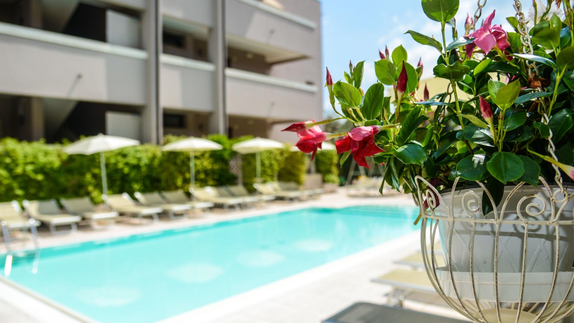 Pool with sun loungers and umbrellas, flowers in the foreground.