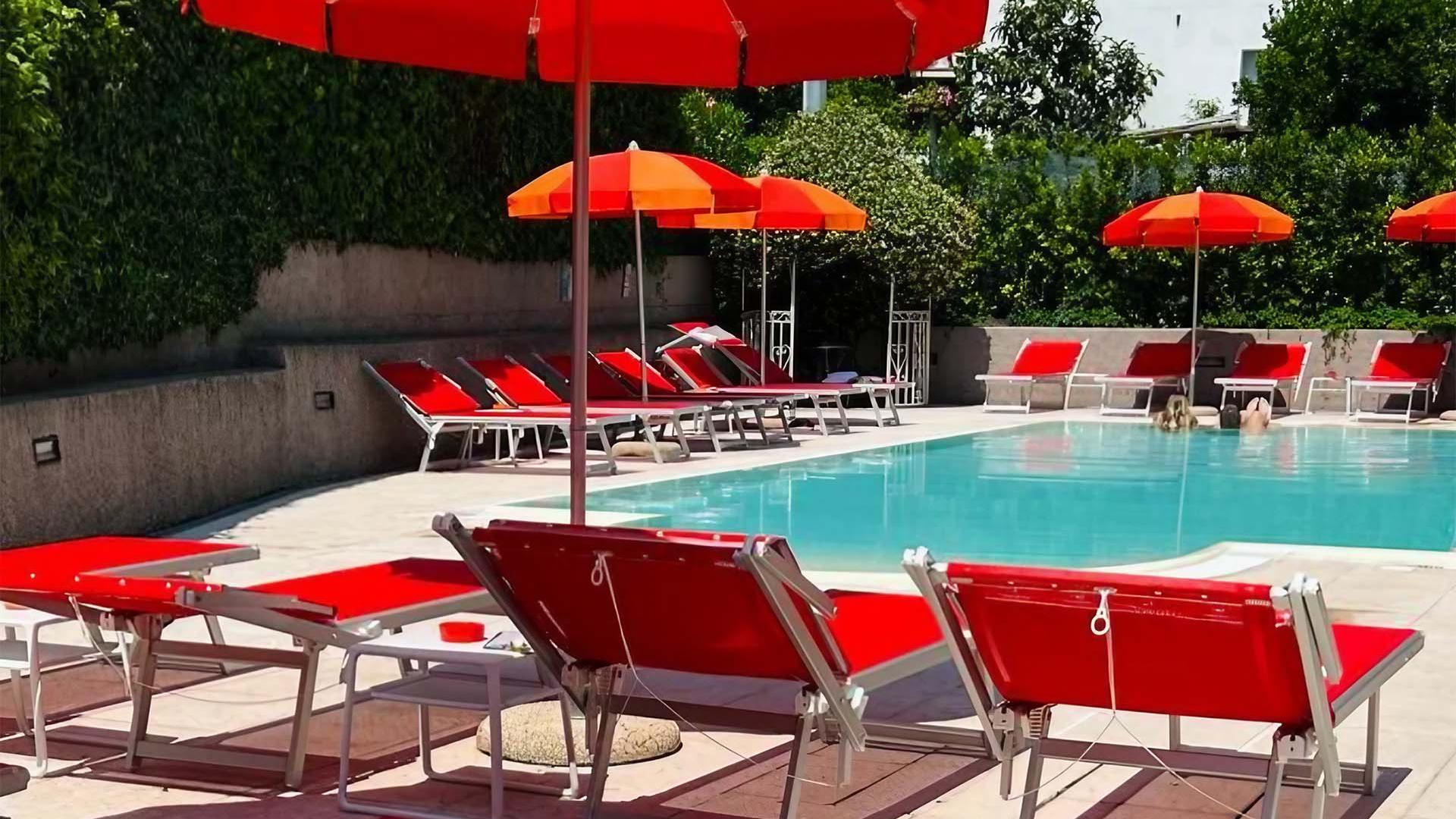 Outdoor pool with red loungers and umbrellas, surrounded by residential buildings.