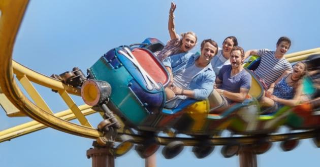 Excited people enjoying a colorful roller coaster ride under a blue sky.