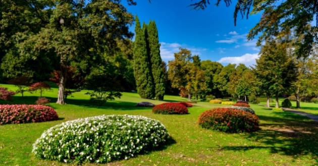 Park with flower beds, lush trees, and clear sky.