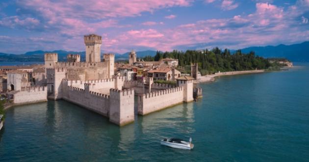 Medieval castle on the lake with boat and sunset sky.