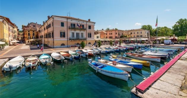 Tourist harbor with colorful boats, historic buildings, and Italian flags.