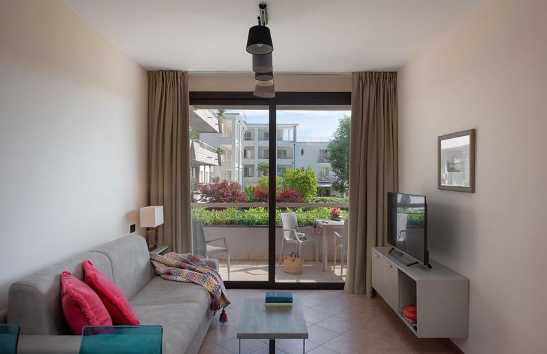 Modern apartment with balcony, TV, gray sofa, and colorful pillows.