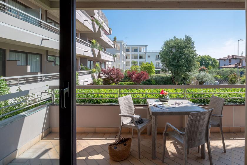 Terrazza con tavolo e sedie, vista su giardino e palazzi moderni.