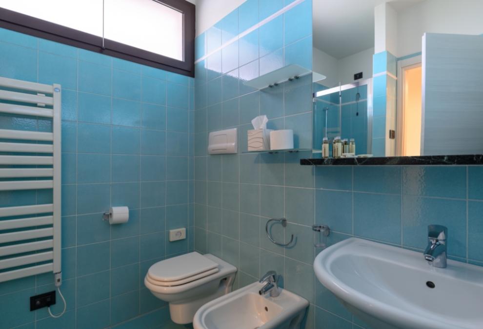 Bagno moderno con piastrelle blu, doccia, lavabo, bidet e wc sospeso.