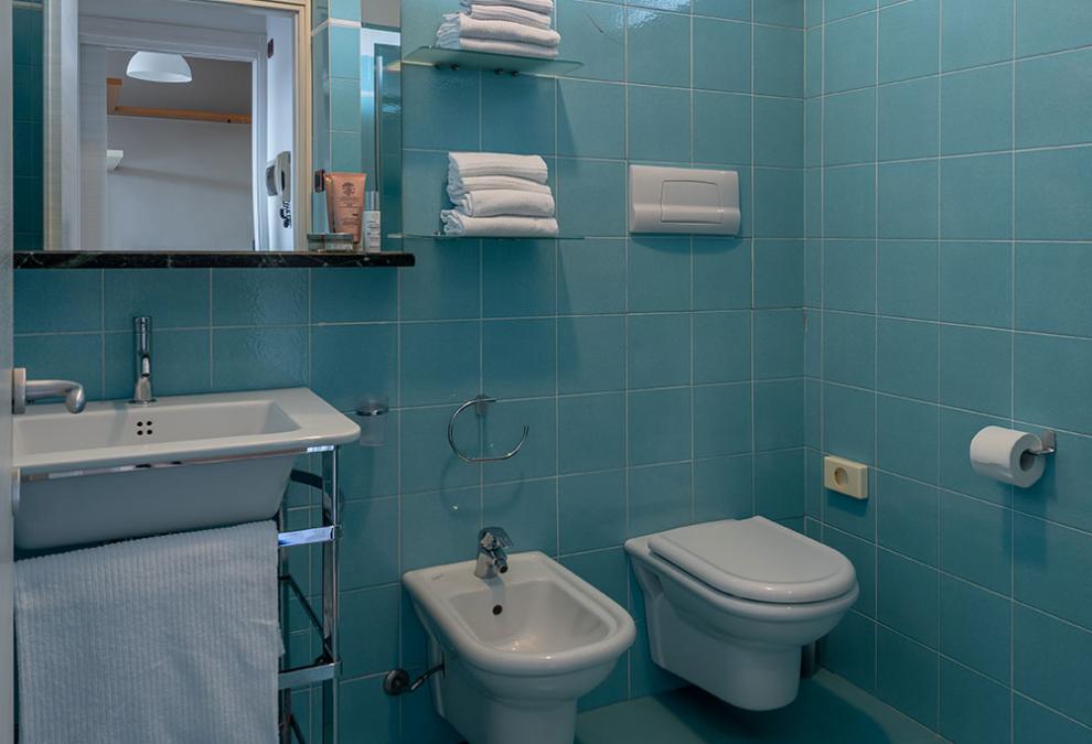 Bagno con piastrelle azzurre, lavabo, bidet e WC, asciugamani sugli scaffali.