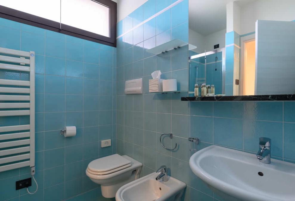 Modern bathroom with blue tiles, white fixtures, and a high window.