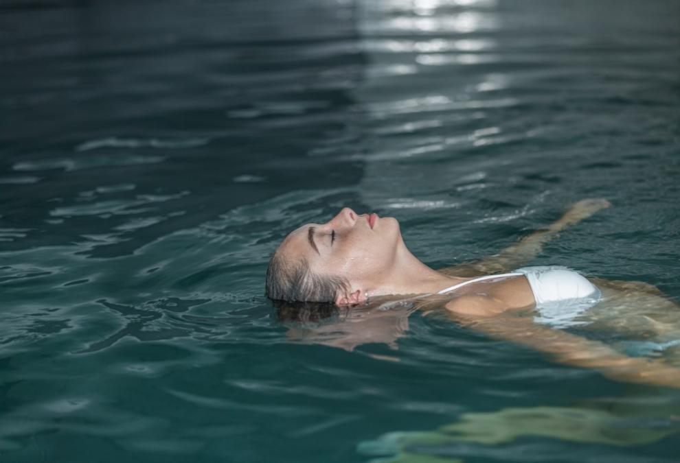 Relaxed woman floating in a pool wearing a white swimsuit.