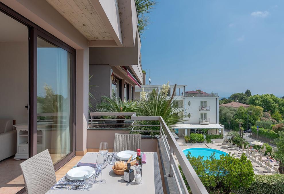 Balcone con tavolo apparecchiato e vista sulla piscina e sul verde circostante.